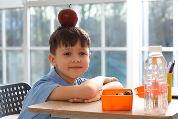 Canvas Print - Cute little schoolboy with apple on his head during lunch in classroom