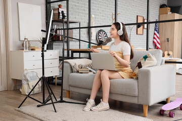 Wall Mural - Female student with laptop and microphone streaming online at home
