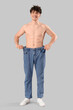 Handsome young happy sporty man in loose jeans on grey background. Weight loss concept