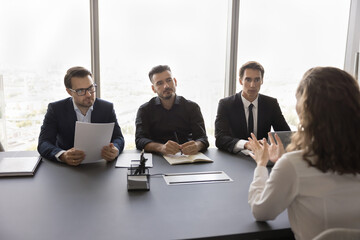 Poster - Rear view of young female applicant sit at desk in front of HR managers, pass job interview, answer questions during formal meeting in conference room. Human resources, qualification, company staffing