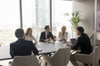 © fizkes - Businesspeople negotiating in conference room in modern city skyscraper office, five businesspeople gathered together, collaborating on problem solving or decision-making processes. Business workflow