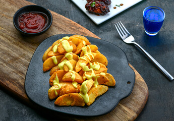 Crispy potato wedges with cheese and tomato sauce on a wooden table with fork