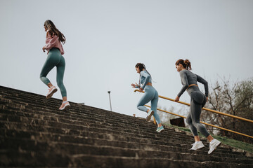 Wall Mural - Outdoor fitness concept with young women running up stairs together, showcasing health and teamwork