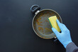 A person in blue gloves cleans a pot with a yellow sponge