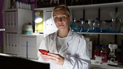 Sticker - Blonde woman in a lab coat examines a smartphone in a laboratory at night, representing technology and healthcare.