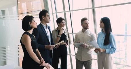 Wall Mural - Multiethnic business team of serious coworkers standing at office large window for briefing, talking, discussing work tasks, teamwork strategy, listening to male Indian boss