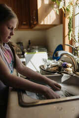 Young girl washes sink full of dirty dishes in kitchen at her home