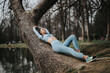 A fit sporty girl takes a break from outdoor exercise, lounging on a large tree in a serene park.