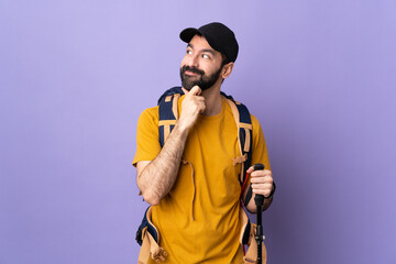 Wall Mural - Caucasian handsome man with backpack and trekking poles over isolated background thinking an idea while looking up
