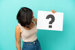 Young mixed race woman isolated on blue background holding a placard with question mark symbol