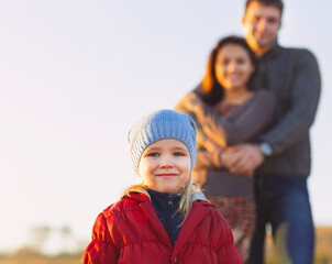 Portrait of the little girl with a funny hat outdoors and man and woman holding hands