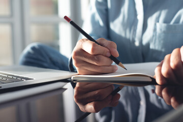 Poster - Woman hand with pencil writing on notebook with laptop computer on office table. Student studying online class and taking note, e-learning, business event planning, to do list reminder