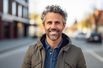 A man with a beard and gray hair is smiling and wearing a green jacket