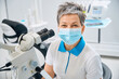 woman oral surgeon in protective face mask sitting near big microscope