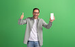 Portrait of young businessman showing thumbs up sign and mobile phone screen on green background