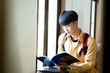 A young man is reading a book while wearing a yellow shirt and a red backpack
