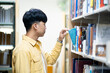 A man in a yellow shirt is looking at a book on a library shelf