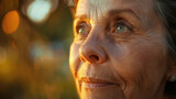 Fototapeta Sport - Close-up of a smiling senior elderly woman's calm and kind face with sunlight shining on the face against a warm background created with Generative AI Technology