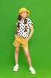 A little girl in a hat and shorts is enjoying the warm summer. Children's summer holidays.  Summer clothes for a child. Green isolated background.