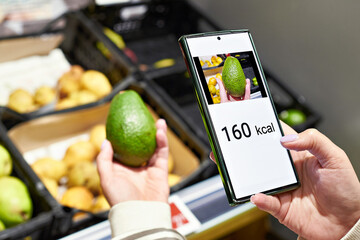 Wall Mural - Checking calories on a avocado fruit in store with smartphone