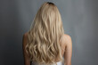 Back view of beautiful woman with long blond wavy hair on a gray studio background.