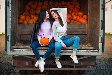 Fashionable beautiful young girlfriends together at the autumn pumpkin patch background. Having fun and posing