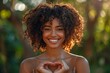 young african - american woman standing and making heart shape with hands in park.