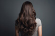 Back view of beautiful woman with long brown wavy hair on a dark gray studio background.
