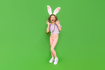 A charming little girl dressed up as an Easter bunny is enjoying the Easter holiday. A full-length child with rabbit ears on his head. Green isolated background. Copy space.