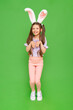 A teenage girl with rabbit ears. A little girl dressed up as an Easter bunny is enjoying a happy Easter holiday. Green isolated background. A full-length child.