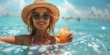 Fototapeta Sport - A stylish, smiling woman relaxes on an inflatable ring in the turquoise sea, sipping a refreshing cocktail.