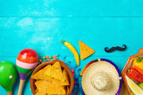 Fototapeta Nowy Jork - Nacho tortilla chips, peppers, maracas and sombrero hat on blue wooden background. Mexican party Cinco de Mayo holiday celebration. Top view, flat lay