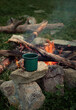 enamel mug with hot drink on big stone near bonfire outdoor.  romantic adventure atmosphere. travel lifestyle, Camping season. lunch break during hiking, trekking, active tourism concept