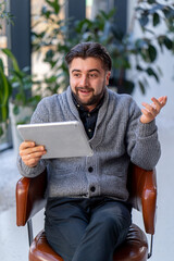 young guy office worker against the background of a window sitting on a chair working with a tablet feeling of victor