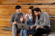 © Guys Who Shoot - three office workers sitting in the lounge area on wooden benches with pillows working a laptop