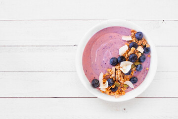 Wall Mural - Healthy blueberry and coconut smoothie bowl with granola. Top view on a white wood background.