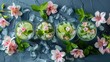  Three glasses of water, each adorned with flowers and ice cubes, sit atop a blue surface Water droplets and additional ice cubes surround them