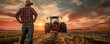 Farmer standing in harvested field with tractor at sunset. Rural agriculture scene with dramatic sky.
