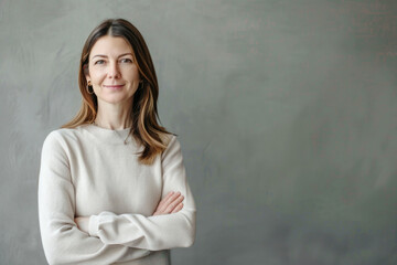 Canvas Print - Portrait of a smiling confident woman in her forties, with crossed arms in front of a grey wall background