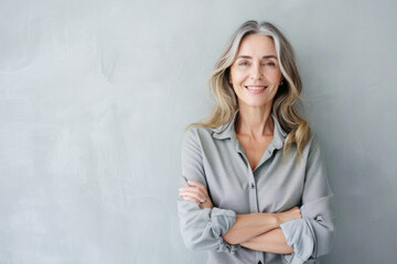 Poster - Portrait of a smiling confident woman in her forties, with crossed arms in front of a grey wall background