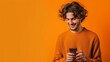 Isolated young man using mobile smart phone on a orange background - Millennial holding cellphone - People and technology concept