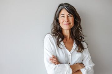 Canvas Print - Portrait of a smiling confident woman in her forties, with crossed arms in front of a grey wall background