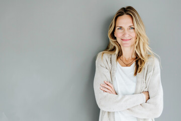 Poster - Portrait of a smiling confident woman in her forties, with crossed arms in front of a grey wall background