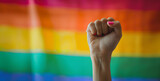 Fototapeta  - A woman protests with her fist raised on gay pride day with the LGBT flag in the background