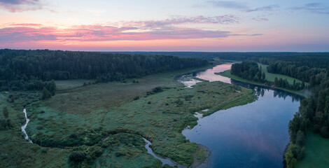 Aufkleber - A river with a beautiful sunset in the background. The water is calm and the sky is filled with orange and pink hues