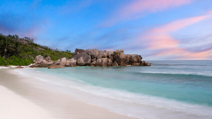 Poster - A rocky shoreline with a calm ocean in the background. The sky is a mix of blue and pink, creating a serene and peaceful atmosphere