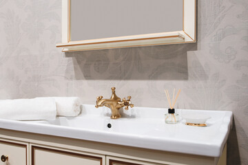 Poster - A bathroom sink with a gold faucet and a white towel on the counter. A vase with a candle and a bottle of perfume on the counter