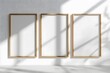 Drei Rahmen im A4-Format stehen nebeneinander auf einer weißen Wand, drei leere Poster, helle Holzrahmen, viel Sonnenlicht