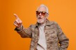 An old man with sunglasses and a casual coat points with confidence against an orange background