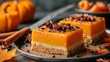   A few slices of cake atop a plate, accompanied by a pair of pumpkins and cinnamon sticks